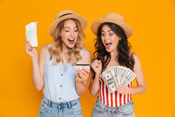 Wall Mural - Portrait of excited women wearing straw hats holding credit card and money bills with passport and travel tickets