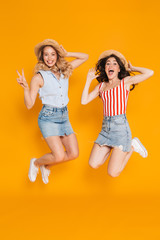 Wall Mural - Portrait of two happy blonde and brunette women 20s in straw hats gesturing peace sing and jumping