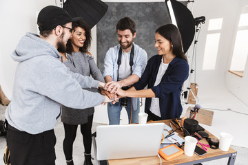 Wall Mural - Portrait of happy multiethnic people making deal while putting hands together during professional photo shooting in studio