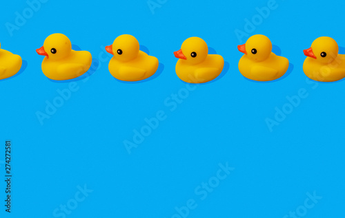 yellow rubber ducks in a row spaced out on blue background with copy space