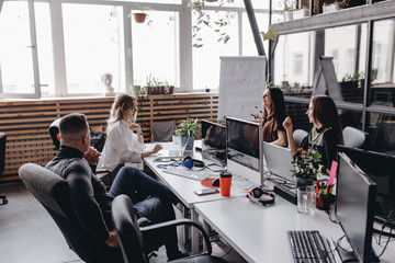 Young team works in a spacious light modern open space office sitting at a desks with a computer and laptops