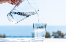 Purified Water Is Poured From A Glass Jug Into A Glass.