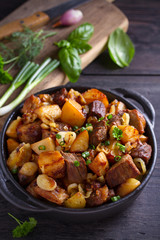 Wall Mural - Fried beef and  potatoes with onions and garlic served in black dish on wooden background