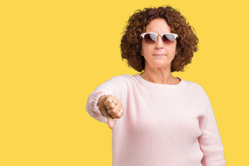 Wall Mural - Beautiful middle ager senior woman wearing pink sweater and sunglasses over isolated background looking unhappy and angry showing rejection and negative with thumbs down gesture. Bad expression.