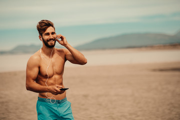 Wall Mural - Handsome man on the beach listens to music over the earphones