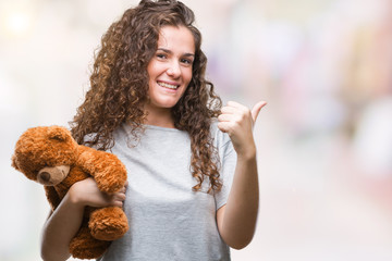 Poster - Young brunette girl holding teddy bear over isolated background happy with big smile doing ok sign, thumb up with fingers, excellent sign