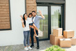 Young happy family standing near the new house. Dad, mom and daughter are waving their hands after buying an apartment.