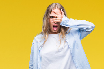 Sticker - Beautiful young blonde woman over isolated background peeking in shock covering face and eyes with hand, looking through fingers with embarrassed expression.