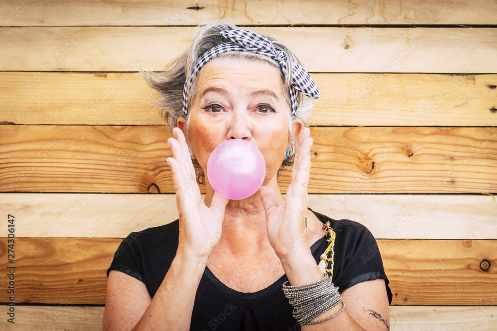 Funny and alternative old people caucasian beautiful woman with pink bubble chewing gum - portrait of youth active senior lady having fun - no limit age lifestyle concept - obrazy, fototapety, plakaty 