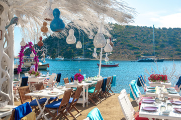 Wall Mural - View of restaurant or cafe and bougainvillea flowers on beach in Gumusluk, Bodrum city of Turkey. Aegean seaside style colorful chairs, tables and flowers in Bodrum town near beautiful Aegean Sea.