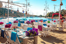 View Of Restaurant Or Cafe And Bougainvillea Flowers On Beach In Gumusluk, Bodrum City Of Turkey. Aegean Seaside Style Colorful Chairs, Tables And Flowers In Bodrum Town Near Beautiful Aegean Sea.