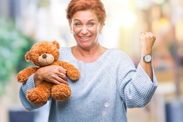 Canvas Print - Senior caucasian woman holding teddy bear over isolated background screaming proud and celebrating victory and success very excited, cheering emotion