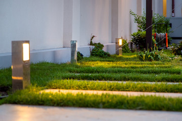 Wall Mural - garden decorative lantern lighting marble walkway in the evening backyard with a green lawn, closeup lantern illumination warm light marble pavement.