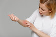 Close up of young woman scratching the itch on her hand, isolated on grey background. Dry skin, animal/food allergy, dermatitis, insect bites, irritation concept. 