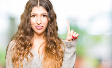 Young beautiful woman wearing winter dress showing and pointing up with finger number one while smiling confident and happy.