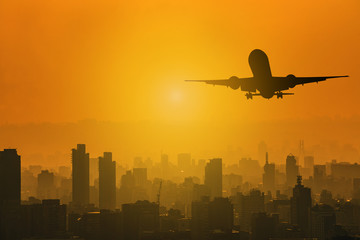 Silhouette of commercial plane flying over a city during with skylight sunset with copy space for text