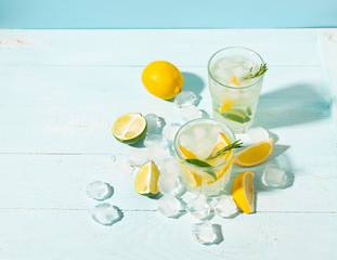 A drink of lemon and lime in an elegant glass on a blue background with bright sunshine. Summer cocktail or mojito.