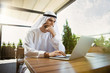 © master1305 - Arab saudi businessman working online with a laptop and tablet in a coffee shop or a cafe with an outdoor terrace in the background. Concept of business, finance, modern technologies, start up.