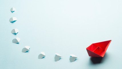 Red origami boat and blue paper hearts in a line behind the boat