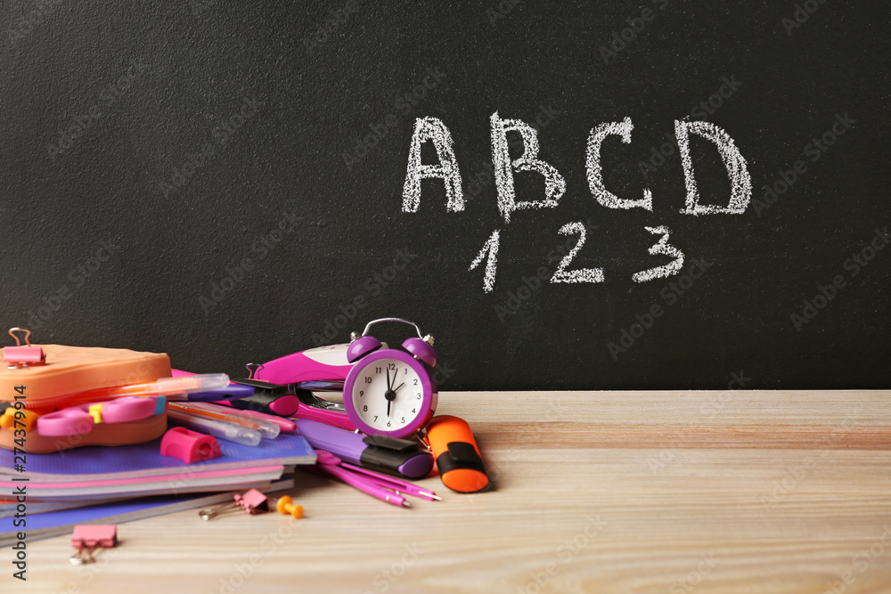 Set of school supplies and clock on table in classroom
