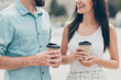 © deagreez - Cropped view photo excited cute spouse fellow fellowship hold hand mug beverage takeout weekend free time tell say speak hear dialogue walk stroll shirt blue denim jeans white dress skirt town outside