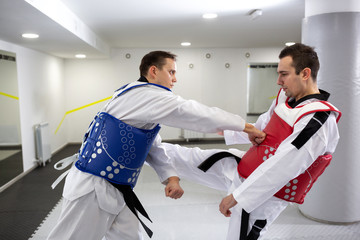 Two men in combat protective gear exchanging punches and kicks