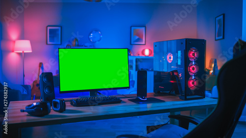 Powerful Personal Computer Gamer Rig with Mock Up Green Screen Monitor Stands on the Table at Home. Cozy Room with Modern Design is Lit with Pink Neon Light.