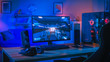 Powerful Personal Computer Gamer Rig with First-Person Shooter Game on Screen. Monitor Stands on the Table at Home. Cozy Room with Modern Design is Lit with Blue and Neon Light.