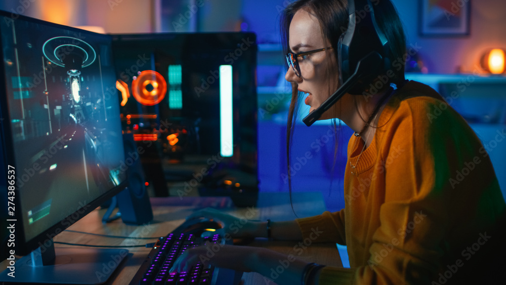 Pretty and Excited Gamer Girl in Glasses and Headset with a Mic Playing Shooter Online Video Game on Her Computer. Room and PC have Colorful Neon Led Lights. Cozy Evening at Home. - obrazy, fototapety, plakaty 