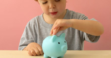 Little Boy Putting Coins In A Piggy Bank At Home