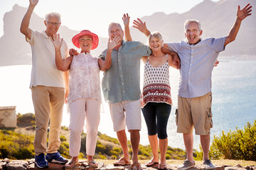 Portrait Of Senior Friends Visiting Tourist Landmark On Group Vacation With Arms Raised