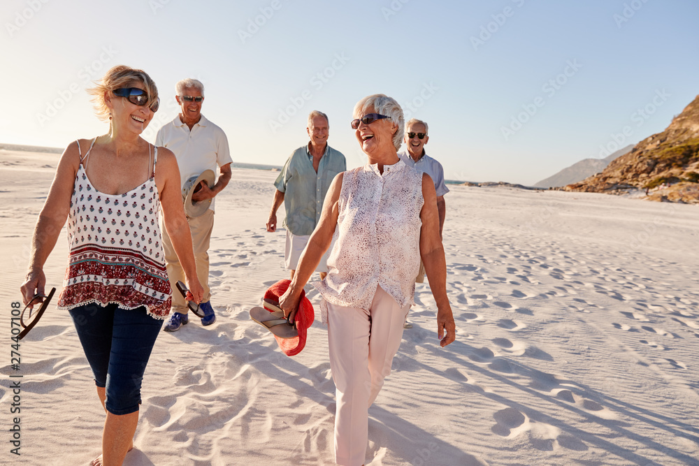 Group Of Senior Friends Walking Along Sandy Beach On Summer Group Vacation - obrazy, fototapety, plakaty 