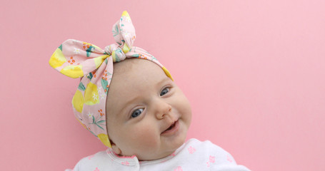 Newborn baby girl smiling in bow pink background