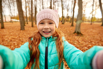 season and people concept - happy girl taking selfie at autumn park