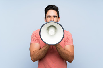 Wall Mural - Handsome young man in pink shirt over isolated blue background shouting through a megaphone