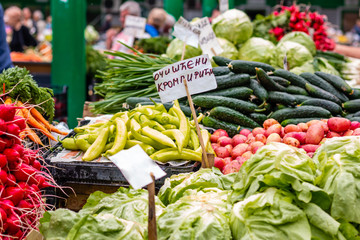 Various fresh vegetables on the marketplace in Belgrade. Blurred sellers and customers on background. Letters 