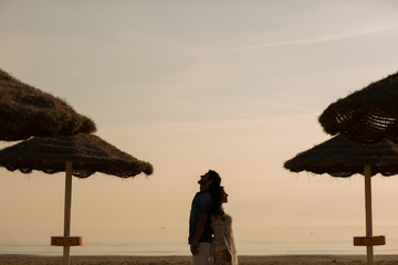 Couple in love having romantic tender moments on the beach near wicker umbrellas. Young lovers enjoying summer vacation