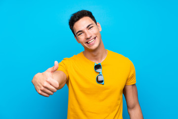 Handsome man over blue background with thumbs up because something good has happened