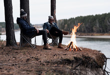 Male Friends Resting Around Bonfire By River