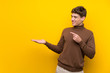 Handsome young man over isolated yellow background holding copyspace imaginary on the palm to insert an ad