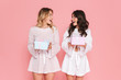Happy young two pretty women girls friends sisters posing isolated over pink wall background holding present boxes.
