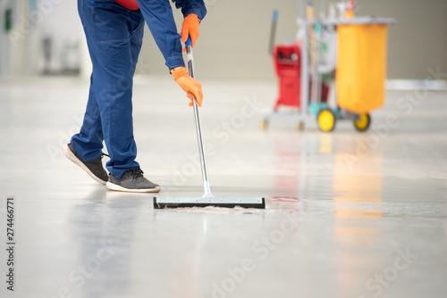 Fotomural The man in the repairman is holding a mop in a white suit, cleaning the protective clothing of the new epoxy floor in an empty warehouse or car service center