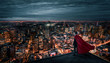 Businessman with red cape like a superhero standing on the rooftop and looking at the city ay night with copy space