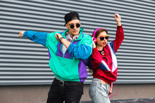 Back In Time 90s 80s. Stylish Young Man In A Retro Jacket And A Girl In Red And With A Vintage Cassette Player, Against A Steel Wall, Fashion Trends, A Street Image
