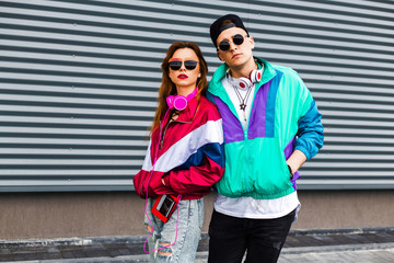 Back in time 90s 80s. Stylish young man in a retro jacket and a girl in red and with a vintage cassette player, against a steel wall, fashion trends, a street image