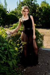 Young attractive woman in the sexy see-through, transparent, transpicuous, diaphanous, clear black dress posing at summer sunny day outdoor in the old park. Fashion woman. Young woman modern portrait.