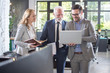 © Bojan - Group of three business people looking something on laptop while standing in modern office