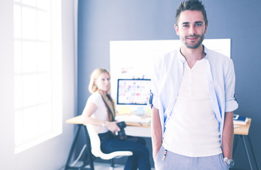 Poster - Portrait of young designer in front of laptop and computer while working. Assistant using her mobile at background.