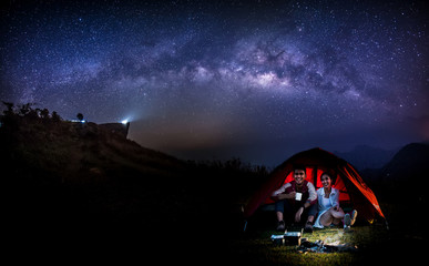 Wall Mural - male and female tourists are in tents on the top of the hill amid the milky way galaxy in the sky. l