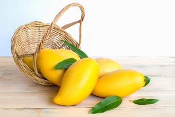 Wall Mural - Ripe mangos and leaves in a basket on woodren floor on white background